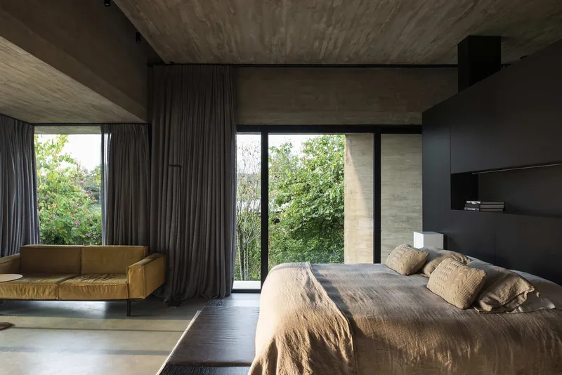 Bedroom with board-formed concrete ceiling and walls overlooking a planted exterior space through glass doors
