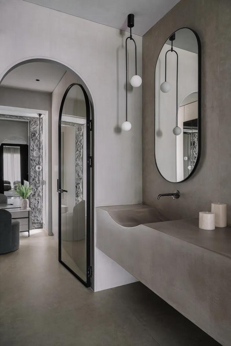 Bathroom vanity with integrated sink in grey stone beneath an arched doorway and pendant lights