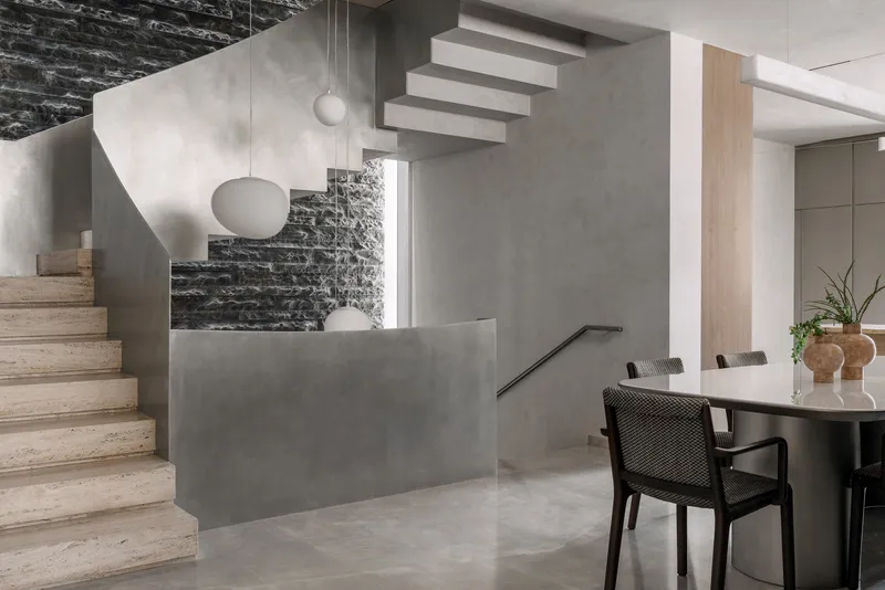 Double-height living space with floating timber staircase and black stone feature wall