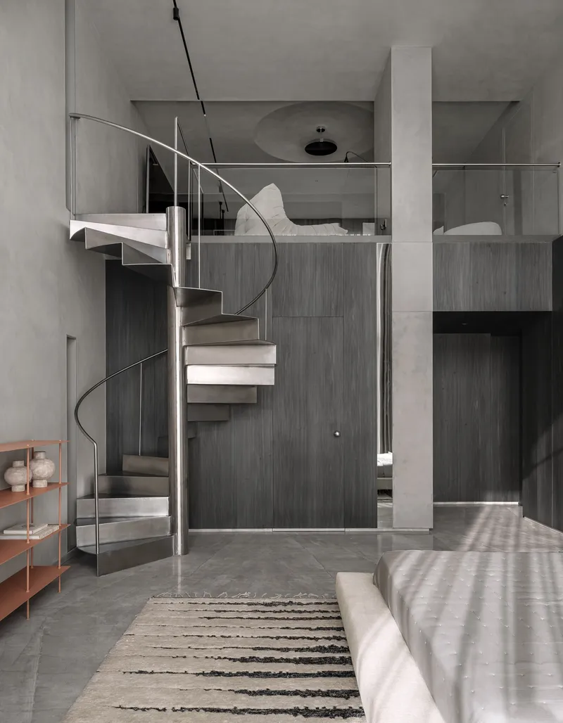 Steel spiral staircase connecting lower bedroom to mezzanine level beneath diffused daylight