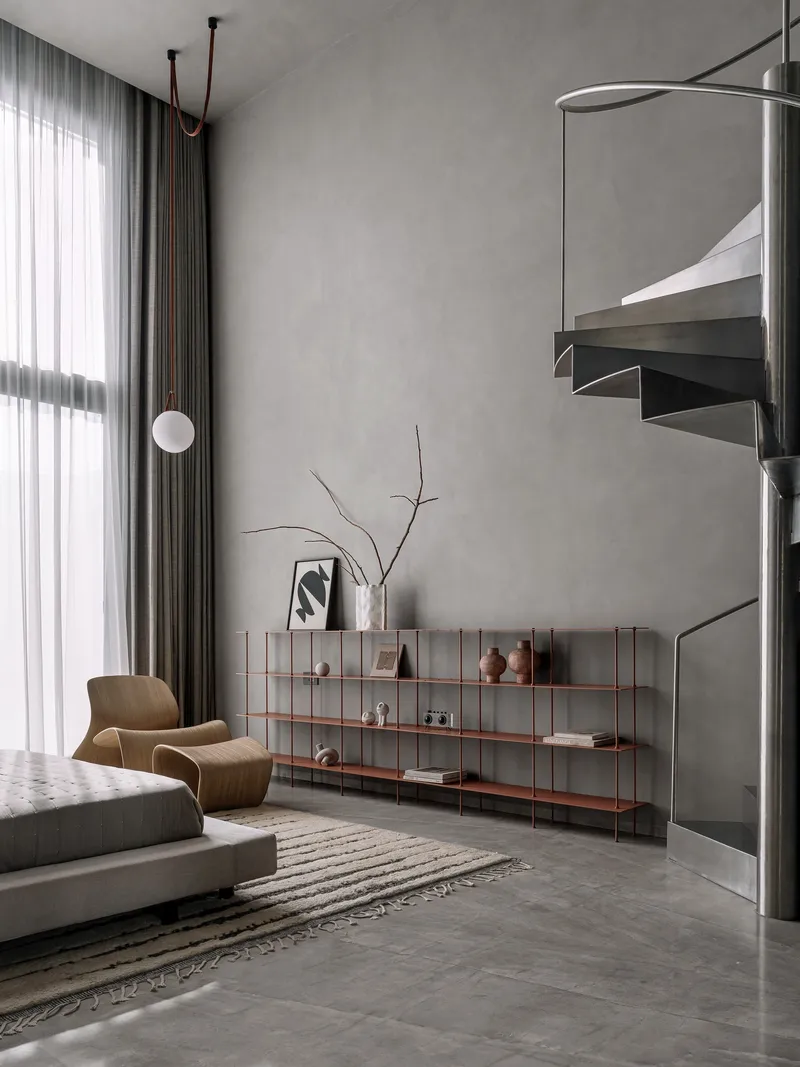 Steel spiral staircase with floating treads beside low shelving unit and grey curtain wall