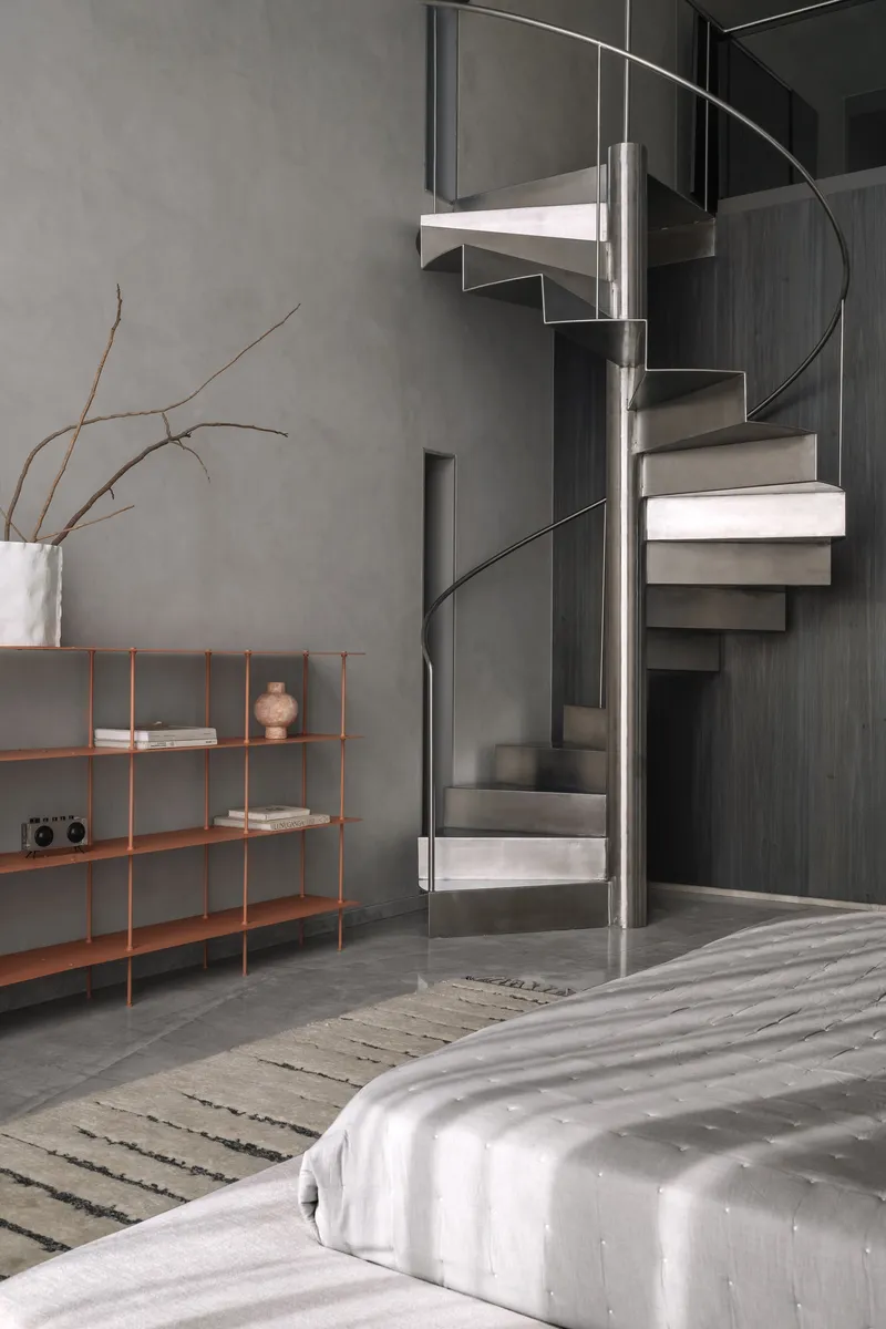 Close-up of circular spiral staircase with metal treads and handrail against dark paneled wall