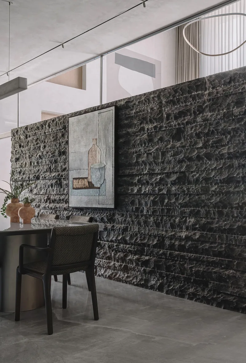Dark split-face stone wall with framed artwork and dining table in soft daylight