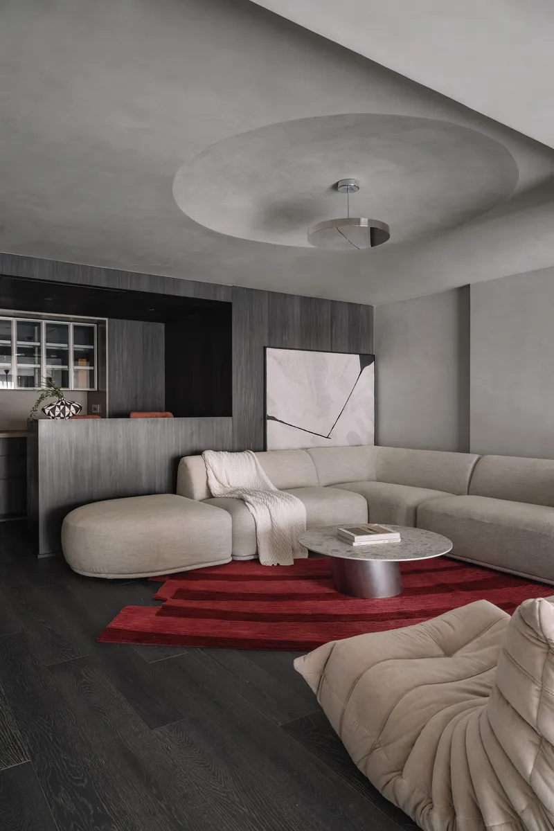 Living room with circular ceiling recess, dark timber millwork, and red geometric rug