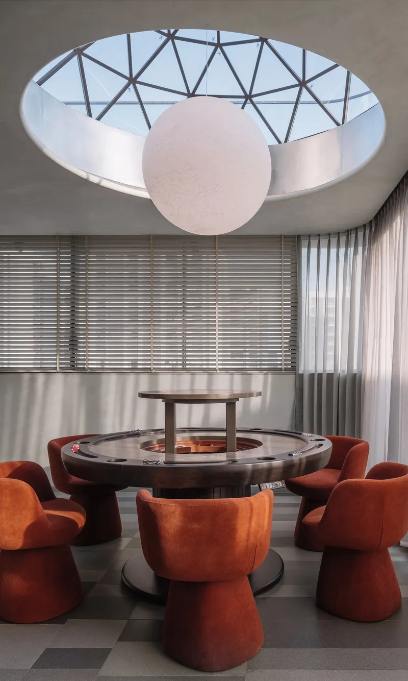 Circular skylight with triangulated steel frame above a round dining table with terracotta upholstered stools