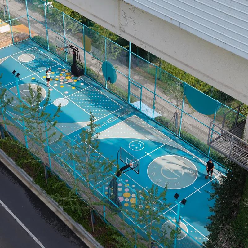 Aerial view of teal sports court with white game markings and scattered play equipment between planted beds