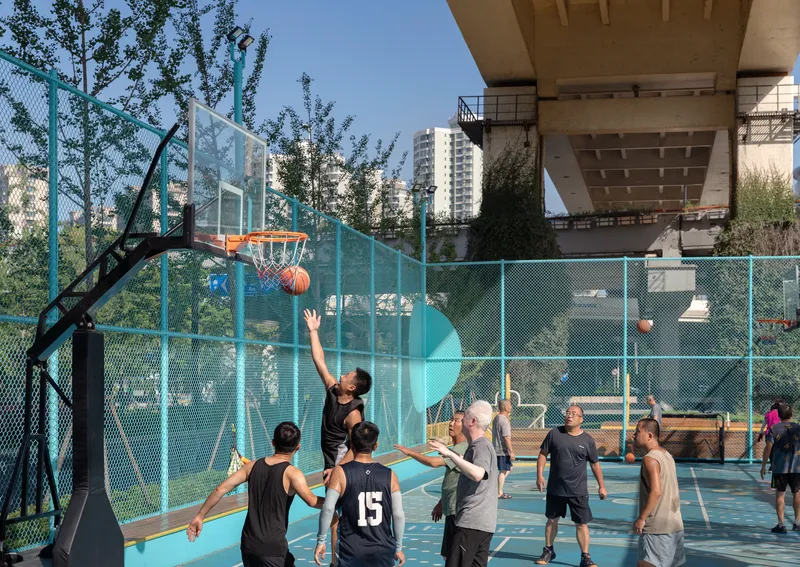 Basketball game in progress on a teal court beneath a concrete elevated roadway at dusk