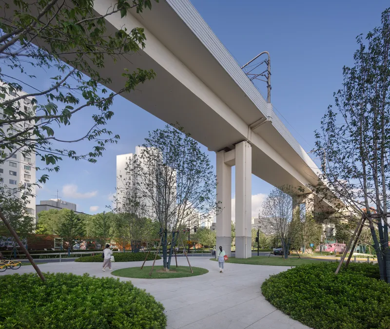 Elevated rail viaduct supported by concrete columns in a landscaped park with walking paths