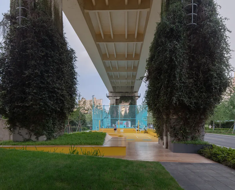 Underside of concrete bridge deck framing lawn and timber pathway between vine-covered support columns at dusk