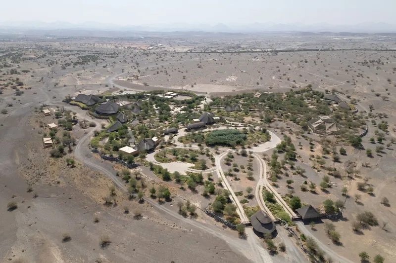 Aerial view of the compound with thatched structures clustered within landscaped grounds in arid terrain