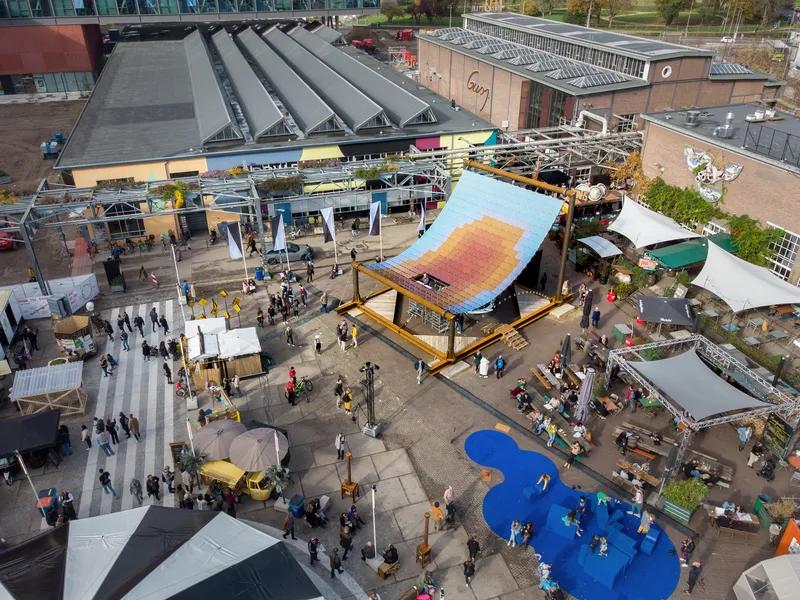 Overhead view of the tilted solar panel canopy structure surrounded by festival tents and visitors in daylight