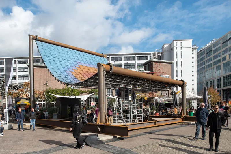 Side view of the gradient solar panel roof supported by timber beams with pedestrians walking beneath on a sunny day