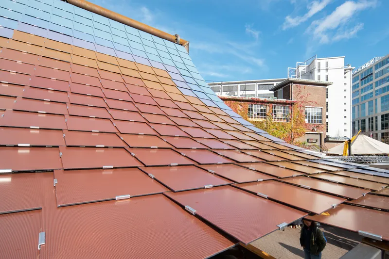 Close-up of the terracotta-toned solar panel array transitioning to blue panels with buildings visible beyond