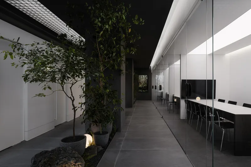 Interior corridor with planted trees in dark gravel beds beside a glazed conference room