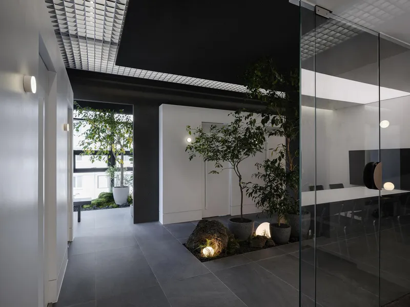 Glass-walled interior garden with planted trees, moss-covered rocks, and a metal mesh skylight