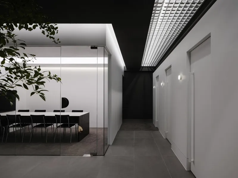 Hallway view toward a glass-enclosed conference room with a metal mesh ceiling panel above