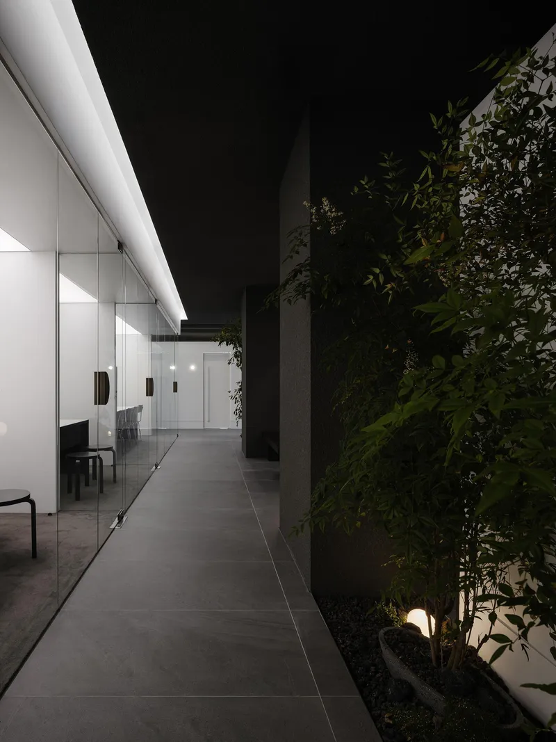 Evening corridor with uplights illuminating a planted green wall and a glazed office beyond