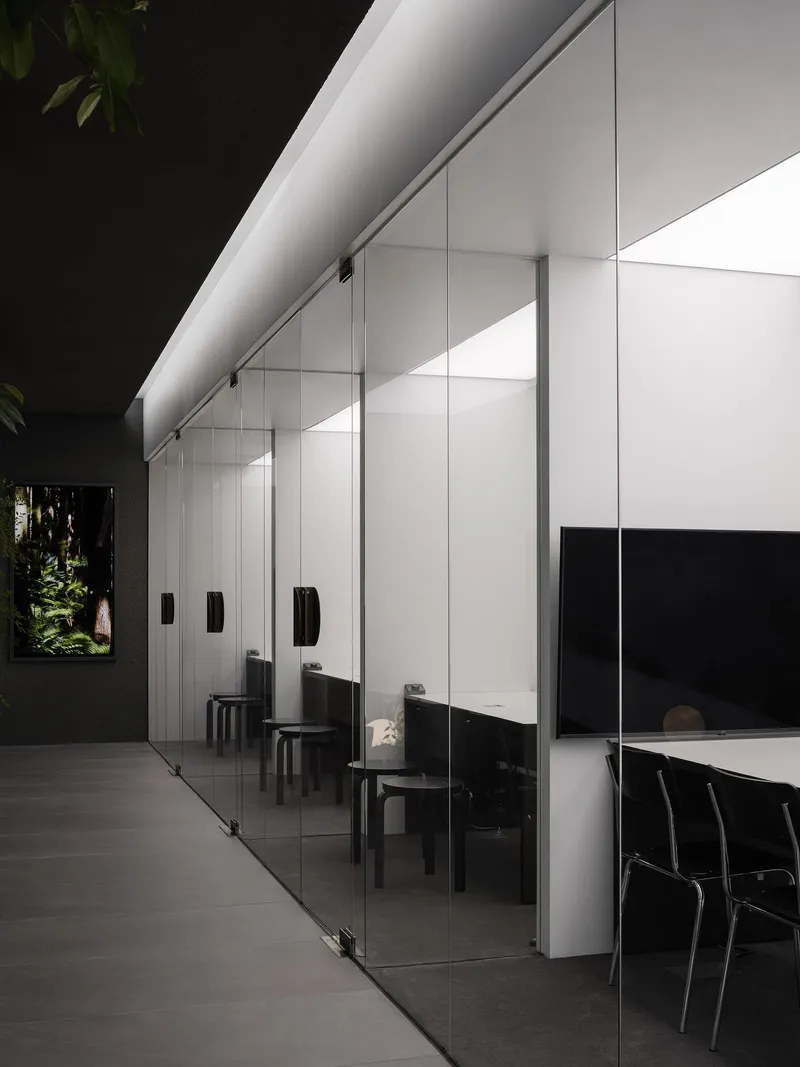Full-height glass partition along the corridor with black-framed doors and uplighting under white soffit