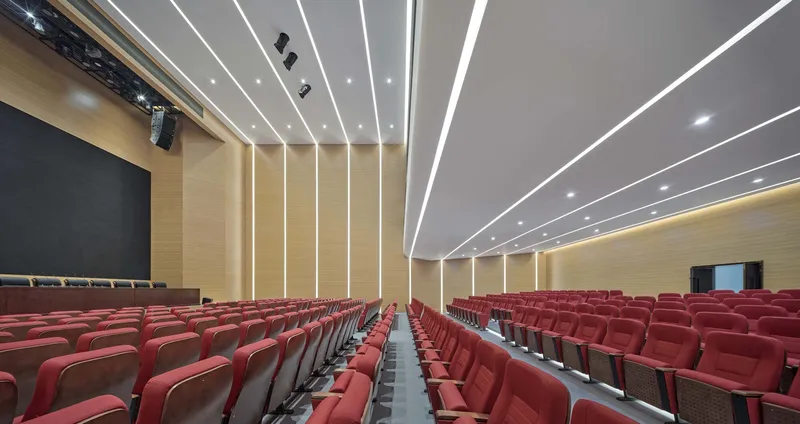 Auditorium interior with red seating rows and linear ceiling light strips