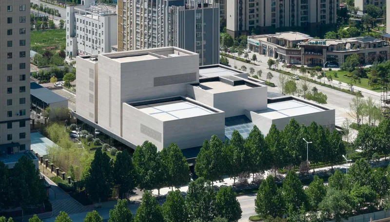 Aerial view of clustered white concrete volumes arranged around a central glass courtyard with tree-lined perimeter
