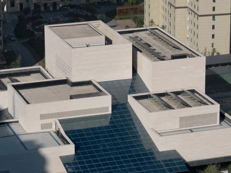Rooftop view showing glass skylight grid connecting white concrete volumes with planted roof terraces