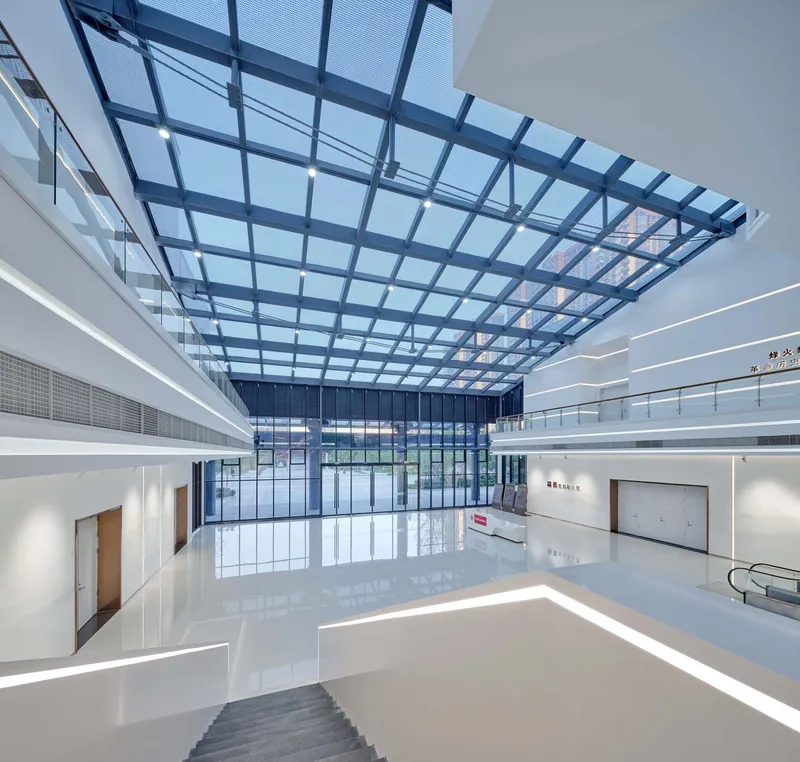 Interior atrium with gridded glass roof above white floors and horizontal light strips on gallery balconies