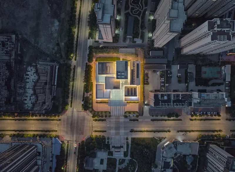 Aerial view at dusk of the illuminated rooftop courtyard surrounded by dense urban blocks