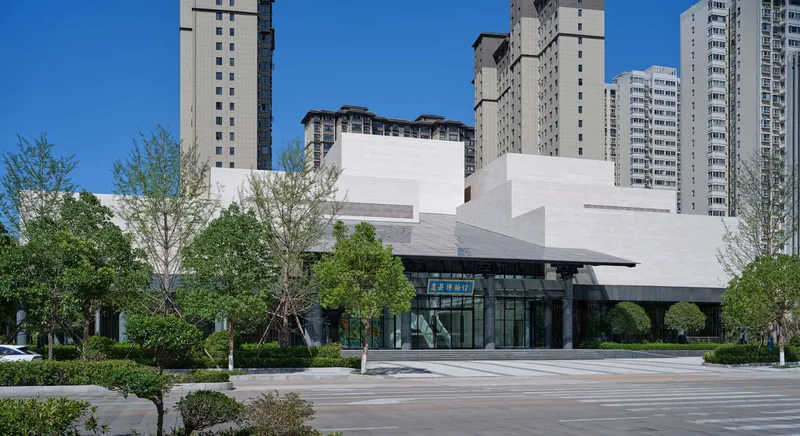 Street view of the glass-walled entrance pavilion beneath stepped white masses and a clear blue sky