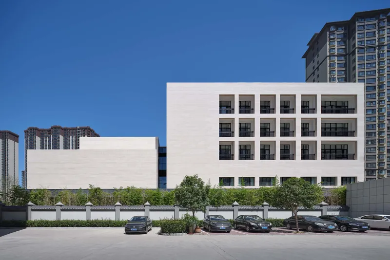 Rear elevation showing grid of square windows in white stone facade with parked cars along the street