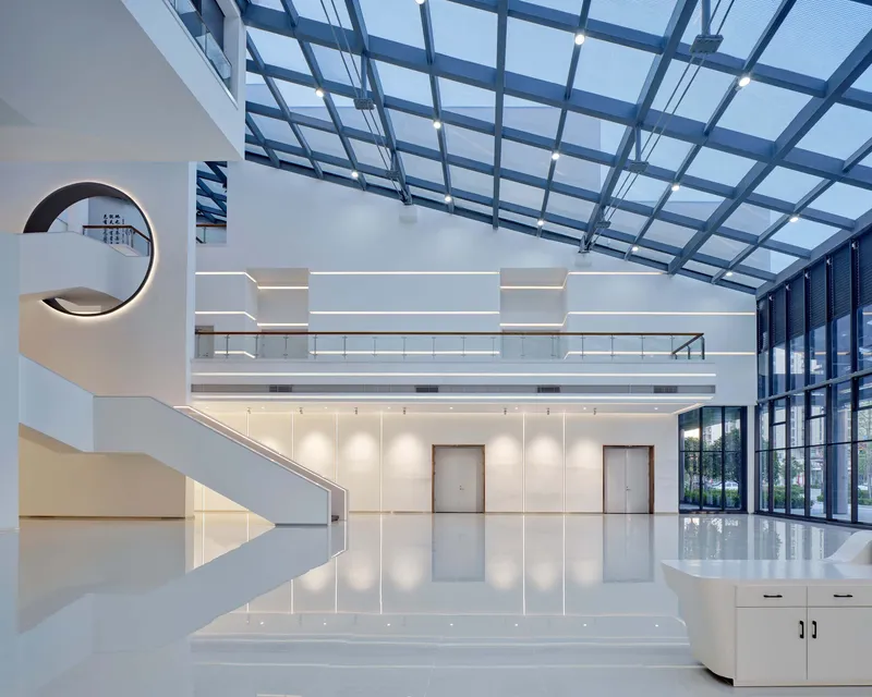 Double-height atrium with curved white staircase, mezzanine level and steel-framed glass roof overhead