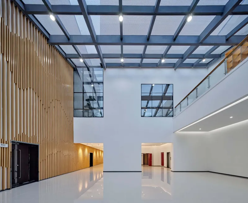 Interior hall with timber slat wall, exposed steel ceiling grid and skylights above polished white floors