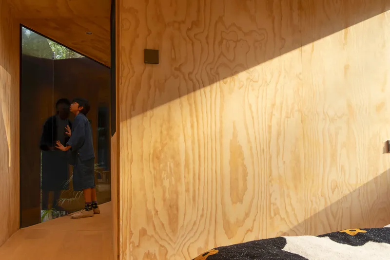 Plywood-lined corridor with angled sunlight casting shadows across the wall and two visitors in the doorway