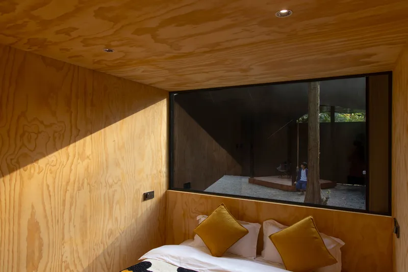 Bedroom with large window framing a view of the gravel courtyard and a figure walking outside