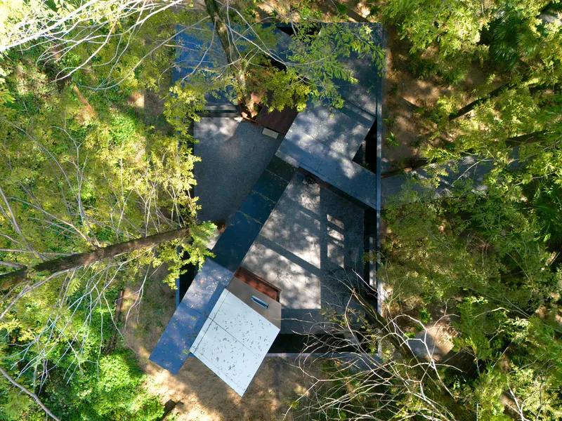 Aerial view of the dark metal roof volumes arranged around gravel courtyards beneath a forest canopy