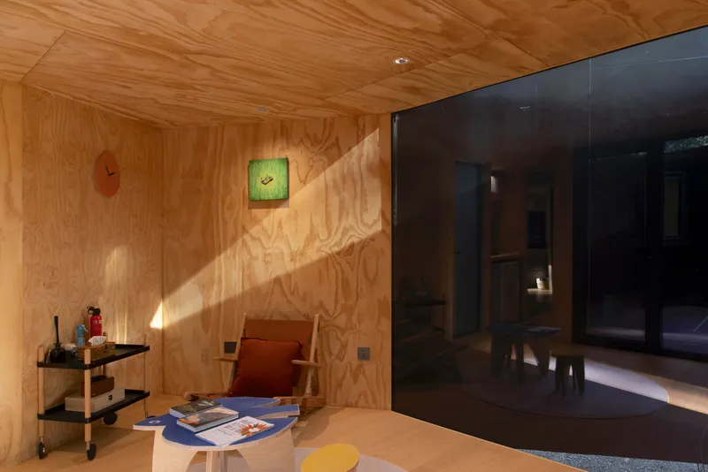 Plywood-lined room with glazed door opening onto a timber deck in afternoon sunlight