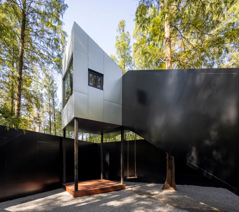 Courtyard with timber swing suspended between two tree trunks beneath the cantilevered white upper volume
