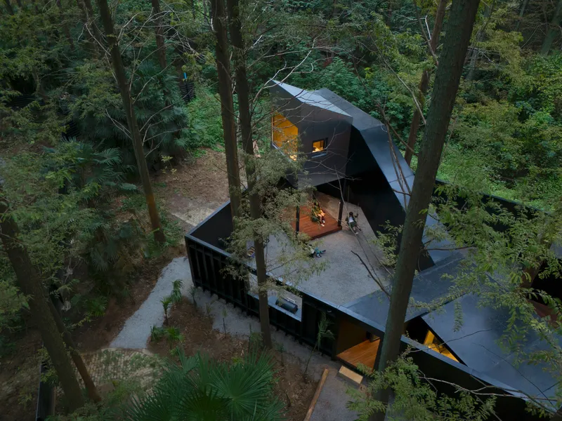 Aerial view of the faceted black metal roofs and concrete courtyard nestled among tall trees at dusk