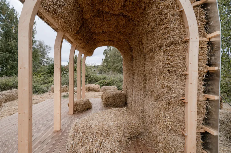 Interior view through the arched straw bale vault with timber columns and scattered bales beyond