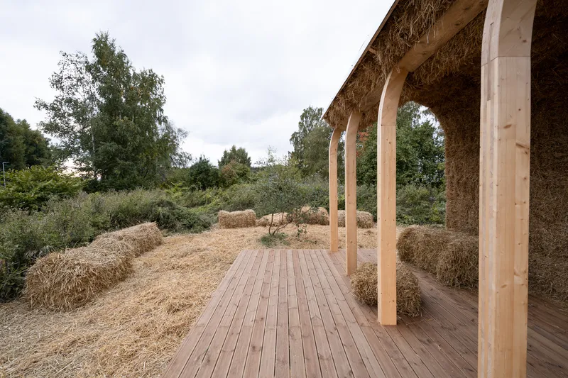 Open pavilion with timber posts and straw bale walls framing views of the surrounding landscape