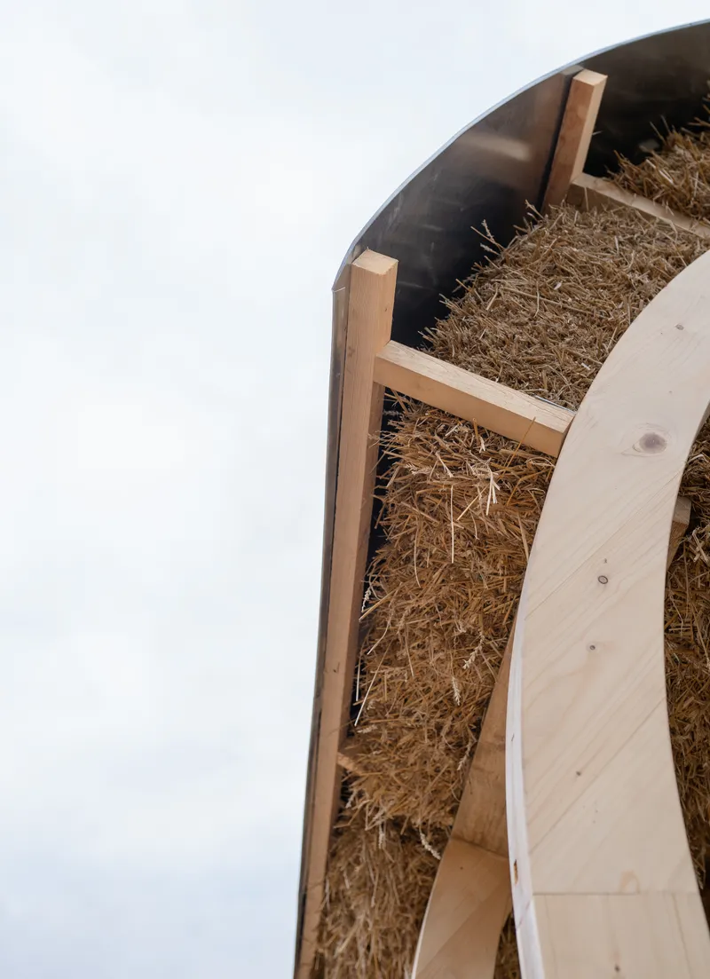 Close-up of curved timber ribs holding straw bale insulation between white exterior cladding