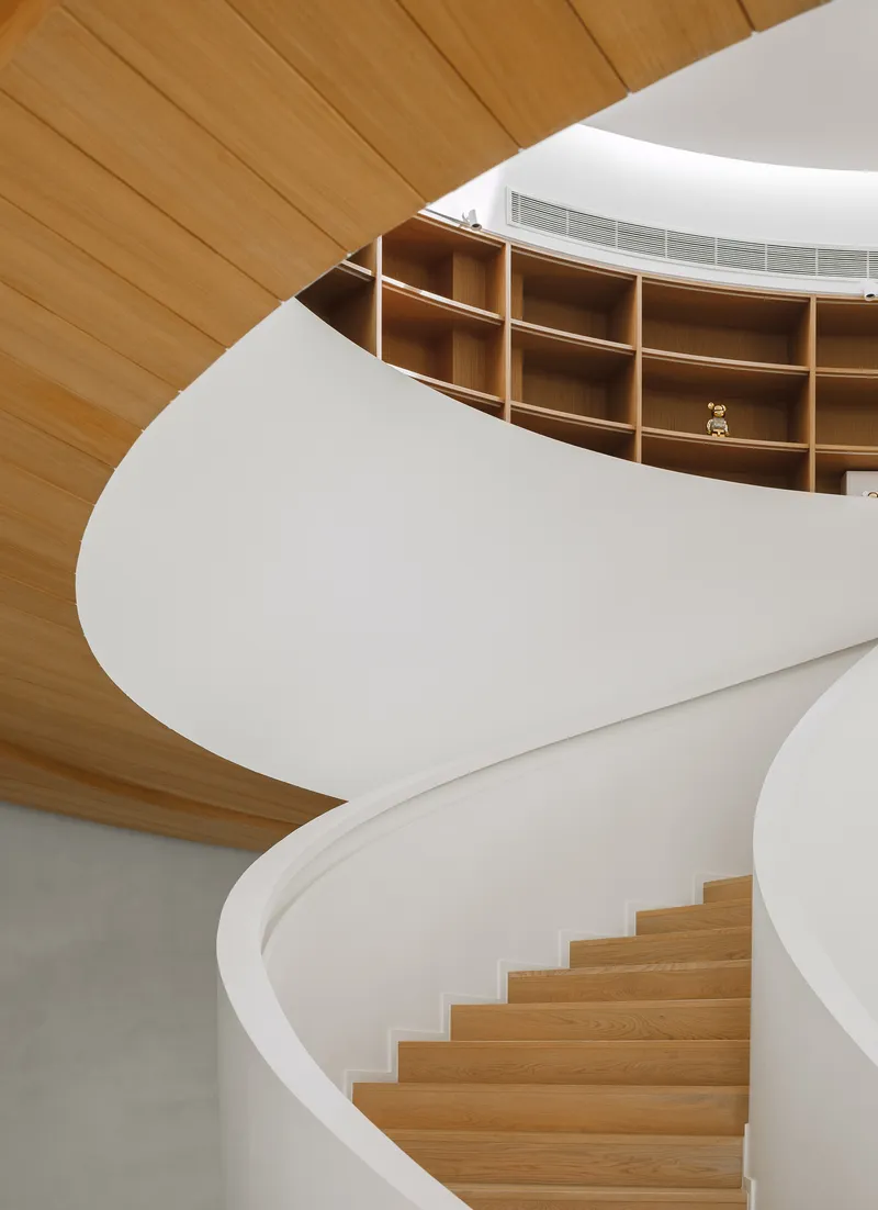 White helical staircase rising through timber-lined ceiling with oak shelving visible on the upper level