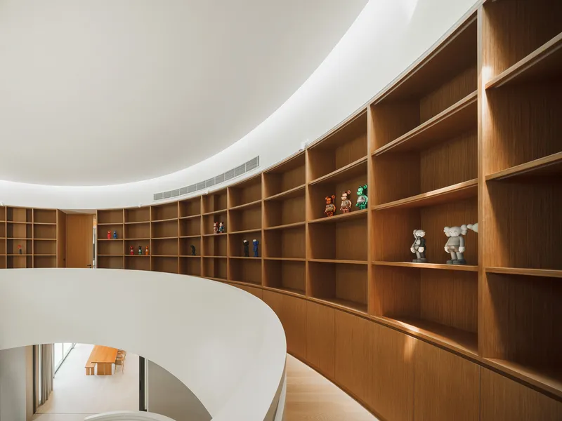 Curved oak shelving wall with collectible toys displayed above the white spiral stair void