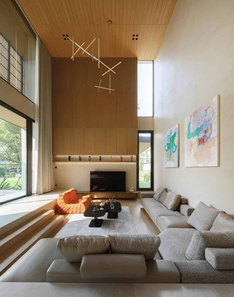 Double-height living room with timber ceiling, stepped seating, and abstract paintings under natural light