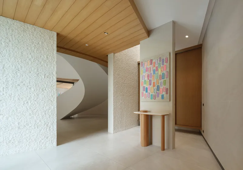 Entry hall with textured white wall, timber ceiling, and spiral staircase beneath indirect lighting