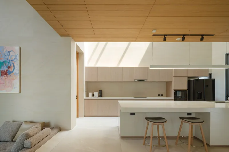 Open kitchen and living area with timber panel ceiling and two wooden stools at the island