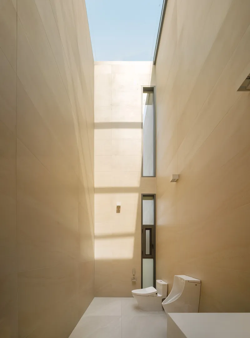 Bathroom with tall skylight shaft drawing natural light down between beige tiled walls