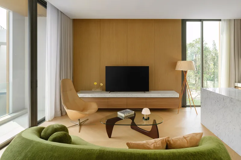 Living room with timber media wall flanked by curtained windows overlooking greenery