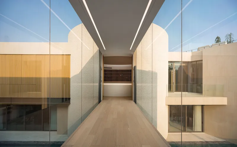 Covered walkway with textured stone walls and linear ceiling lights under afternoon sun