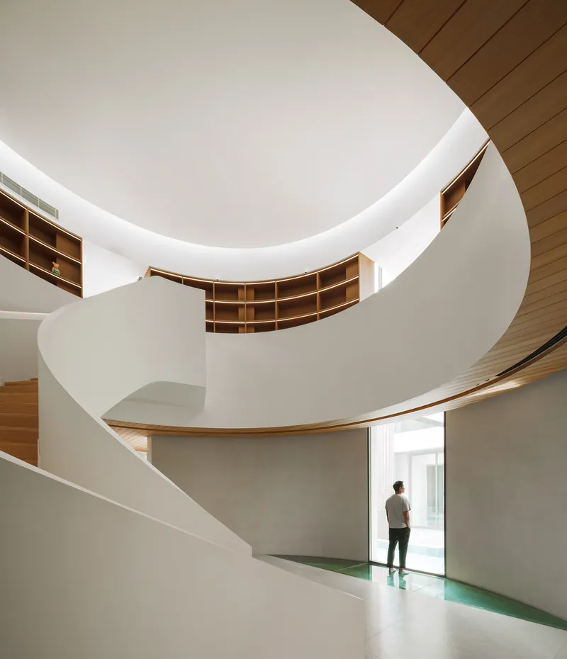 Multi-storey spiral staircase with timber shelving and a person walking below
