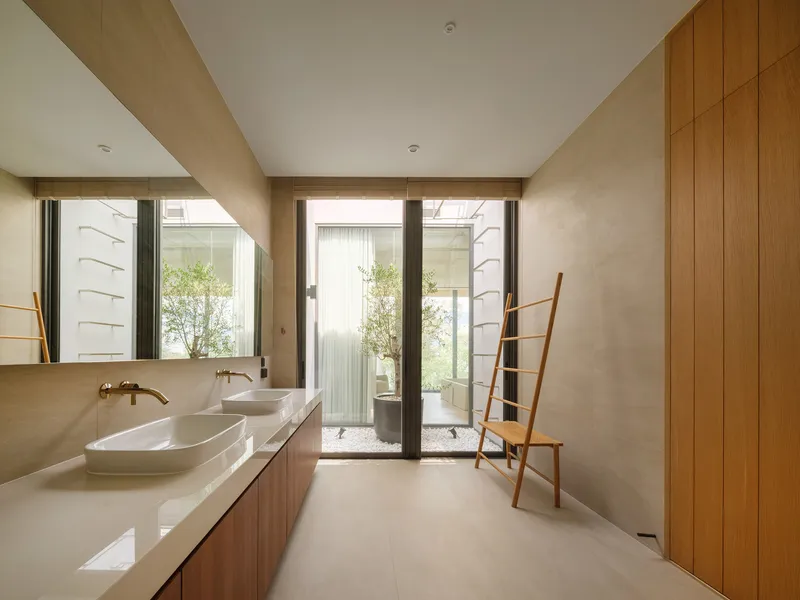 Bathroom with timber vanity and vertical wood panels framing glazed doors to a courtyard with trees